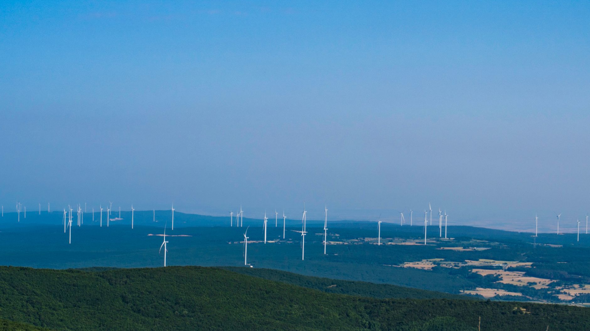 Wind turbines operating on rolling green hills under a bright sky.
